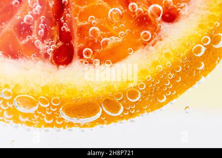 Grapefruit close-up in liquid with bubbles. Slice of blood red ripe grapefruit in water. Part of set. Stock Photo