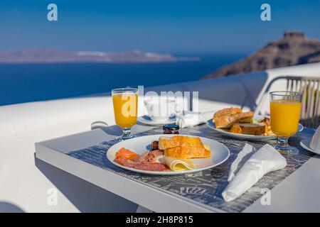 Breakfast table romantic view under idyllic blue sky sea. Perfect luxury breakfast food table for two outdoors. Amazing caldera view on Oia Santorini Stock Photo