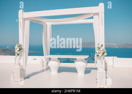 Santorini Island, Greece. Wedding decoration on a popular couple destination. Elegant wedding arch with white flowers, vases on background of blue sea Stock Photo