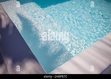 Abstract swimming pool background. Summer relax and recreational concept, blue ripped water with stairs in swimming pool, sunny blurry waves. Stock Photo