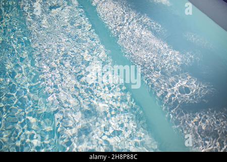 Abstract swimming pool background. Summer relax and recreational concept, blue ripped water with stairs in swimming pool, sunny blurry waves. Stock Photo