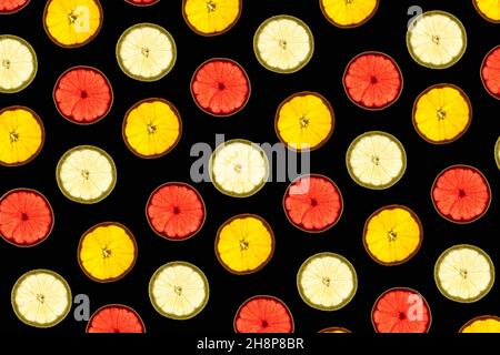 Pattern made of backlit citrus fruits slices on black background Stock Photo