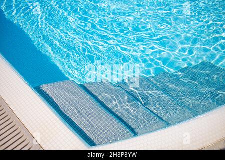 Edge of blue swimming pool. Summer water sport, recreational background. Texture of water surface, blue turquoise vivid bright sunny closeup stairs Stock Photo