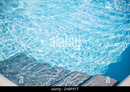 Edge of blue swimming pool. Summer water sport, recreational background. Texture of water surface, blue turquoise vivid bright sunny closeup stairs Stock Photo