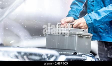 Car technician replaces dead car battery in winter conditions. Stock Photo