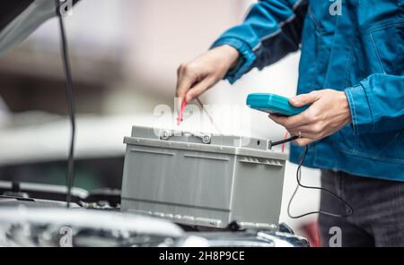 Car repaid garage technician checks lifespan of a car batery with a multimeter. Stock Photo