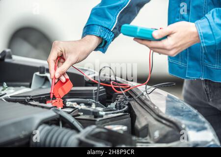 Car electrician or mechanic checks voltage in car battery inside the car engine with open hood. Stock Photo