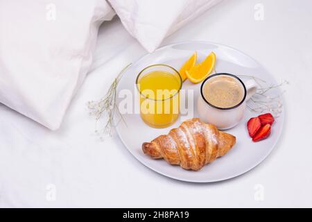 Romantic morning breakfast in bed. Orange juice, croissant and strawberry on the plate. Stock Photo