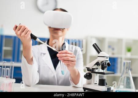 Test tube and electronic pipette in hands of blurred scientist in vr headset working in lab Stock Photo