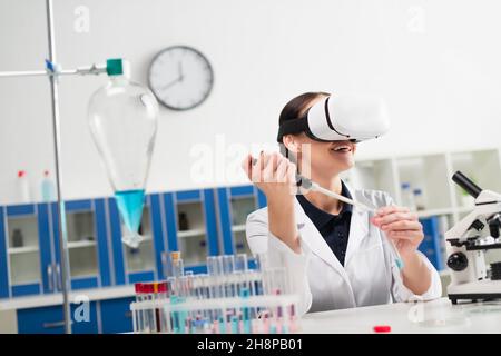 Cheerful scientist in vr headset working with test tube and electronic pipette in lab Stock Photo