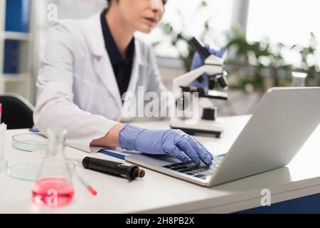 Cropped view of blurred scientist in latex gloves using laptop near equipment Stock Photo