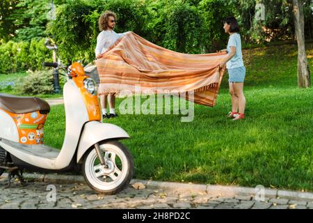 Happy smiling young multiethnic couple holding blanket standing on green grass in park Stock Photo