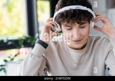 Smiling young transgender person using headphones in office,stock image Stock Photo