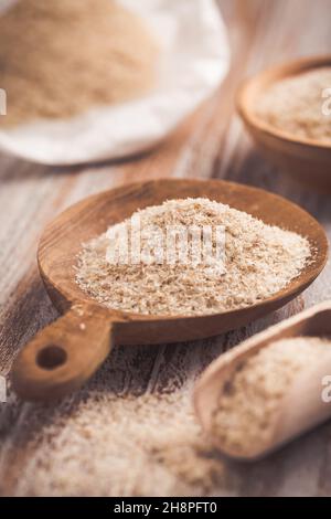 Heap of psyllium husk in wooden bowl on wooden table table. Psyllium husk also called isabgol is fiber derived from the seeds of Plantago ovata plant Stock Photo