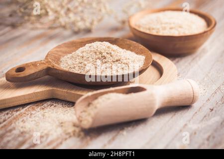 Heap of psyllium husk in wooden bowl on wooden table table. Psyllium husk also called isabgol is fiber derived from the seeds of Plantago ovata plant Stock Photo