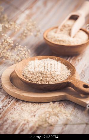 Heap of psyllium husk in wooden bowl on wooden table table. Psyllium husk also called isabgol is fiber derived from the seeds of Plantago ovata plant Stock Photo