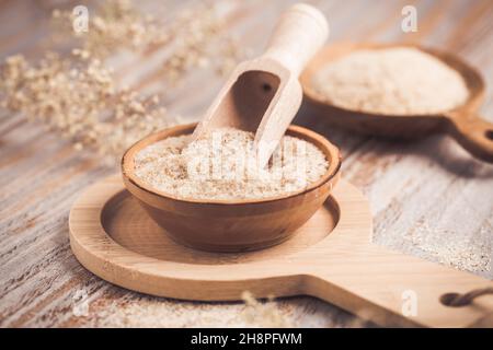 Heap of psyllium husk in wooden bowl on wooden table table. Psyllium husk also called isabgol is fiber derived from the seeds of Plantago ovata plant Stock Photo