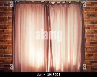Window with closed beige curtains in the loft room close up. View from the room to a window illuminated by daylight from the outside Stock Photo