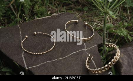 Three modern golden bracelets on natural rock between grass with copy space Stock Photo