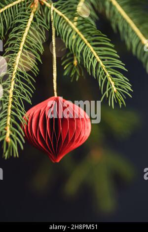 Red Christmas honeycomb paper decoration on fir branch. Stock Photo