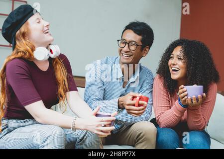 multiracial group of friends having a coffee together, two women and a man laughing and talking at cafeteria, real people having fun during breakfast Stock Photo