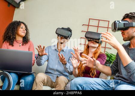group of young friends experiencing virtual reality with headset, one woman piloting the AR, experienced influencers and players trying a new virtual Stock Photo