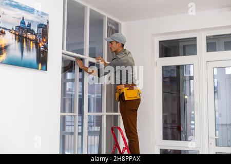 Construction worker installing metal profile for interior partition wall, while building a new house or renovation process, viewed from his back. Stock Photo