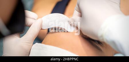 The beautician is gluing a patch under her eyes, before the procedure of eyelash extension. Artificial extended eyelashes Stock Photo