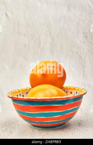 Persimmon in a orange and green color bowl on white background.
