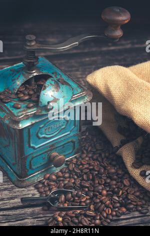 jute bag and coffee beans on old wooden table. Coffee concept., Vertical high angle detail studio shot of still life with vintage manual green metal Stock Photo