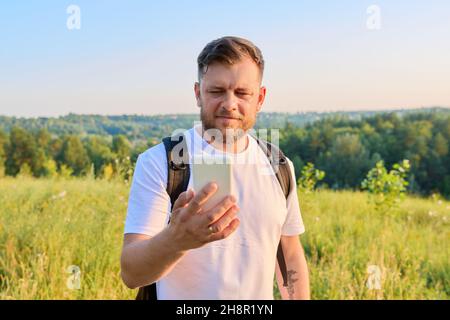 Middle-aged bearded man with backpack using smartphone Stock Photo