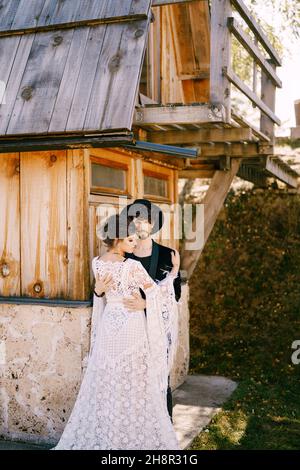 Groom hugs bride in a white lace dress near the old wooden house Stock Photo