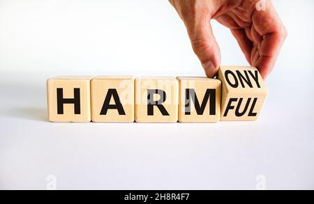 From harmful to harmony. Businessman turns the wooden cube and changes word harmful to harmony. Beautiful white table, white background. Business and Stock Photo