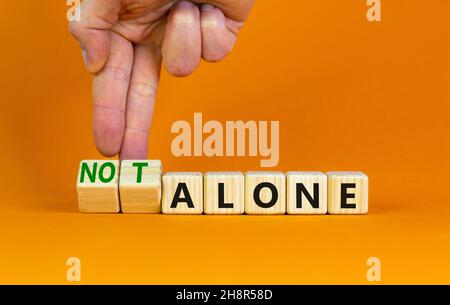 You are not alone symbol. Businessman turns wooden cubes and changes words alone to not alone. Beautiful orange table orange background, copy space. B Stock Photo