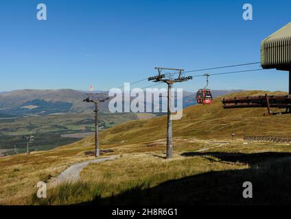 Nevis Range cable car red gondola approaching the top station on a clear sunny day with blue sky, hills and walkers in background Stock Photo