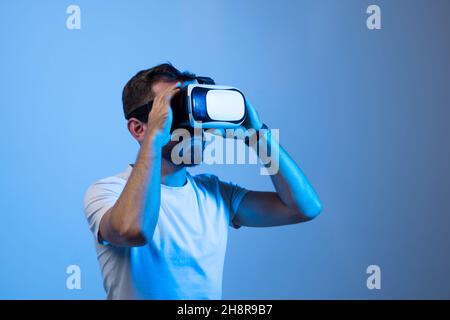 Attractive young man in black t-shirt wearing virtual reality headset or 3d glasses. Handsome male using VR headset and playing video games. Stock Photo