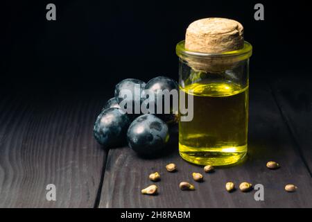 Grape oil seed in small bottle. Heap of grape seeds with blue grapes and cold press organic essential oil, tincture, extract, infusion on wooden rusti Stock Photo