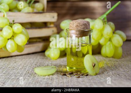 Grape oil seed in small vintage bottle. Heap of grape seeds with green grapes and cold press organic essential oil, tincture, extract, infusion on woo Stock Photo