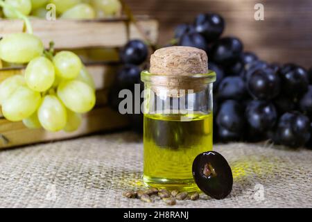 Grape oil seed in small vintage bottle. Heap of grape seeds with green grapes and cold press organic essential oil, tincture, extract, infusion on woo Stock Photo