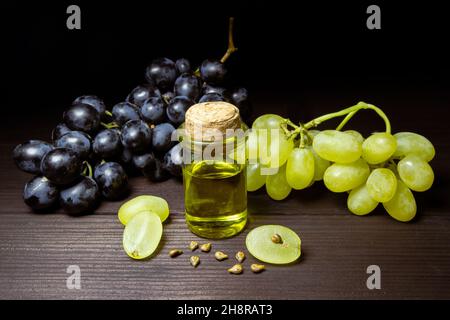 Grape oil seed in small vintage bottle. Heap of grape seeds with green grapes and cold press organic essential oil, tincture, extract, infusion on woo Stock Photo