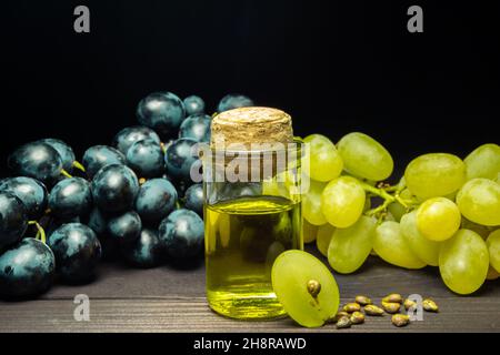 Grape oil seed in small vintage bottle. Heap of grape seeds with green slices and cold press organic essential oil, tincture, extract, infusion on Stock Photo