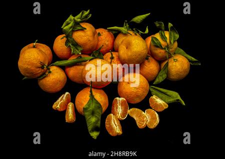 Peeled slices with ripe tangerines, with dark green leaves lie in a group on a black background Stock Photo