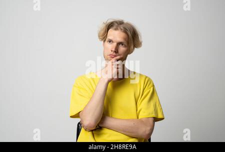 Portrait of thoughtful young man who looks away and touching his chin and weighs the pluses and minuses of the offer isolated on white background with Stock Photo
