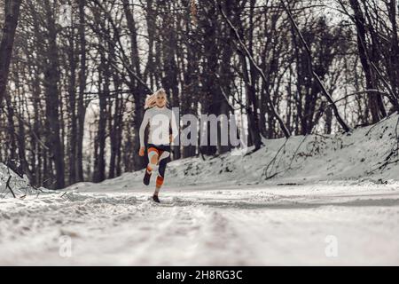 Fit sportswoman running on snowy path in nature at winter. Sports, cardio exercises, winter fitness Stock Photo