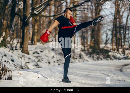 Strong muscular fighter with boxing gloves sparring in nature at snowy winter day. Boxing, winter fitness Stock Photo