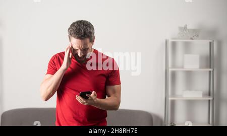 shocked man reading message on phone in office interior, copy space, bad news Stock Photo