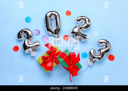 Figure 2023 made of silver balloons, gift boxes and confetti on blue background Stock Photo