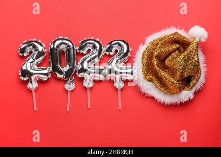 Figure 2022 made of silver balloons and Santa Claus hat on red background Stock Photo