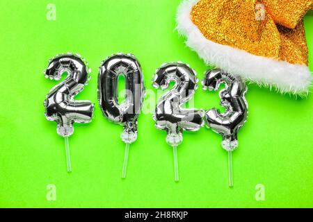 Figure 2023 made of silver balloons and Santa Claus hat on green background Stock Photo