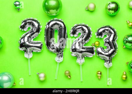 Figure 2023 made of silver balloons and Christmas balls on green background Stock Photo